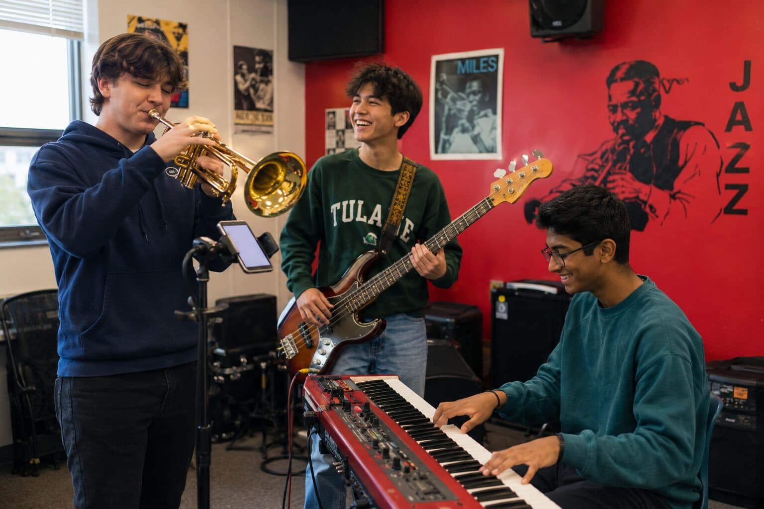 Three young musicians playing trumpet, bass, and keyboard together in a rehearsal room.